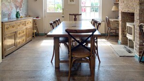 A dining area with a wooden table and chairs, a map on the wall, and a bookshelf filled with books. - Coastguard's Cottage (Burnham Overy Staithe, near Burnham Market)
