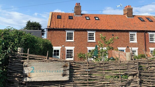 A traditional brick building with a tiled roof, multiple windows, and a wooden fence in the foreground. - Coastguard's Cottage (Burnham Overy Staithe, near Burnham Market)
