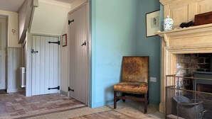 A hallway with a wooden floor, a chair, a fireplace, and a door. - Coastguard's Cottage (Burnham Overy Staithe, near Burnham Market)