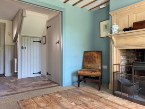 A hallway with a wooden floor, a chair, a fireplace, and a door. - Coastguard's Cottage (Burnham Overy Staithe, near Burnham Market)