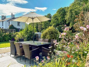 Eine Terrasse im Freien mit Korbmöbeln und einem Tisch unter einem Sonnensegel.