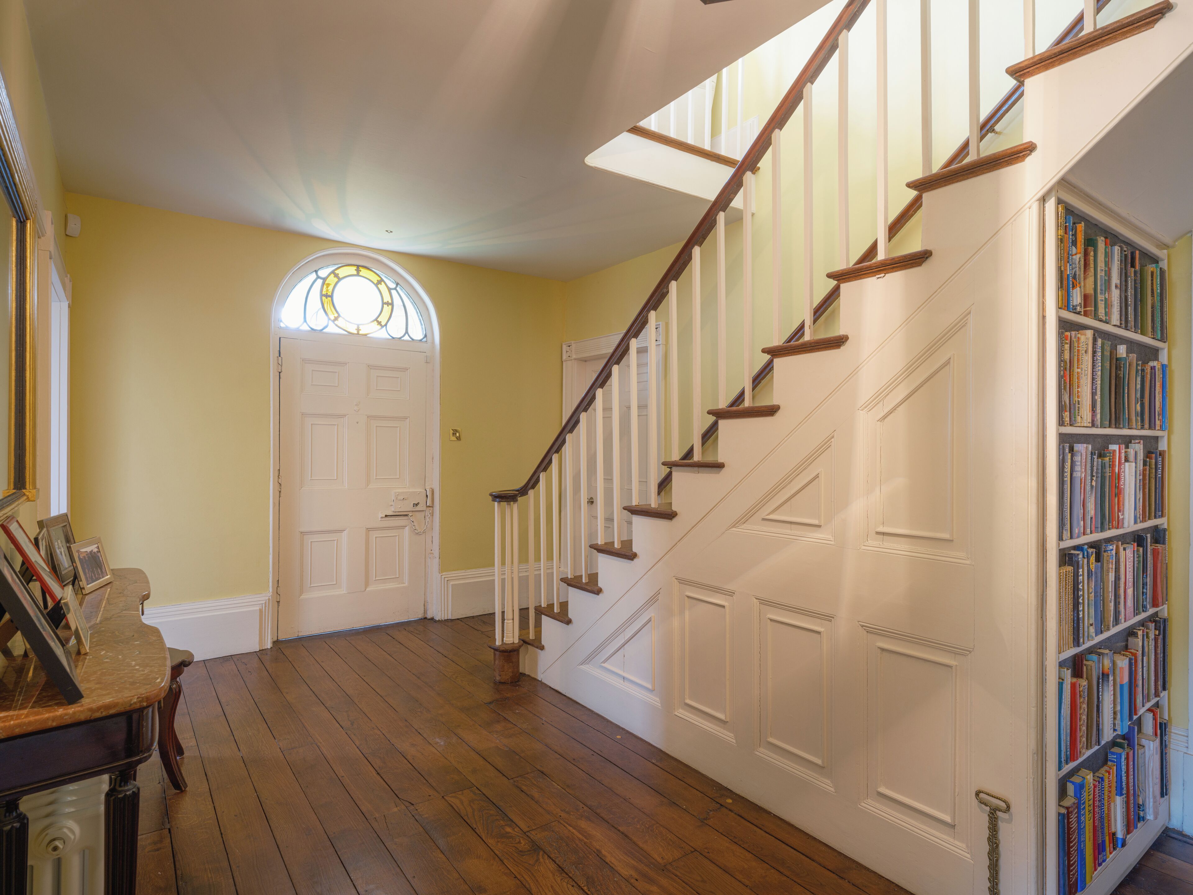 A staircase with wooden steps and white railings, leading to a door with a stained glass window above.