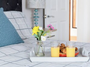 Ein Frühstücksbrett mit Orangensaft und Gebäck auf einem Bett mit einem gemusterten Bettüberwurf.