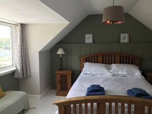 A bedroom with a sloped ceiling, a bed with white linens and blue towels, a wooden nightstand with a lamp, and two framed pictures on the wall. - 4 bedroom accommodation in Fowey (Fowey)