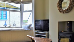 En hyggelig stue med fjernsyn, pejs og et vindue med udsigt til en blå bygning.