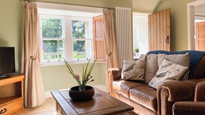 Una sala de estar acogedora con un sofá de cuero, una mesa de centro de madera con un jarrón y un televisor sobre un mueble de madera.