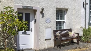 Une petite maison blanche avec une pancarte indiquant « La maison de Mary » et un banc à l’extérieur.