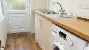 A compact kitchen with a washing machine, a sink, and a wooden countertop. - 2 bedroom accommodation in Keswick (Keswick)