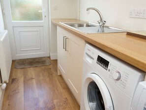 Une cuisine de taille réduite, équipée d’un lave-linge, d’un évier et d’un plan de travail en bois.