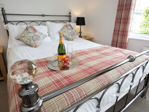 A neatly made bed with a plaid bedspread, a bottle of champagne, and a bowl of strawberries on a tray. - 2 bedroom accommodation in Keswick (Keswick)