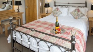 A neatly made bed with a checkered bedspread, a bedside table with a bottle and glasses, and a wooden nightstand with a lamp. - 2 bedroom accommodation in Keswick (Keswick)