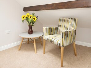 Ein Zimmer mit einem runden weißen Tisch, einem gestreiften Sessel und einer Vase mit Sonnenblumen.