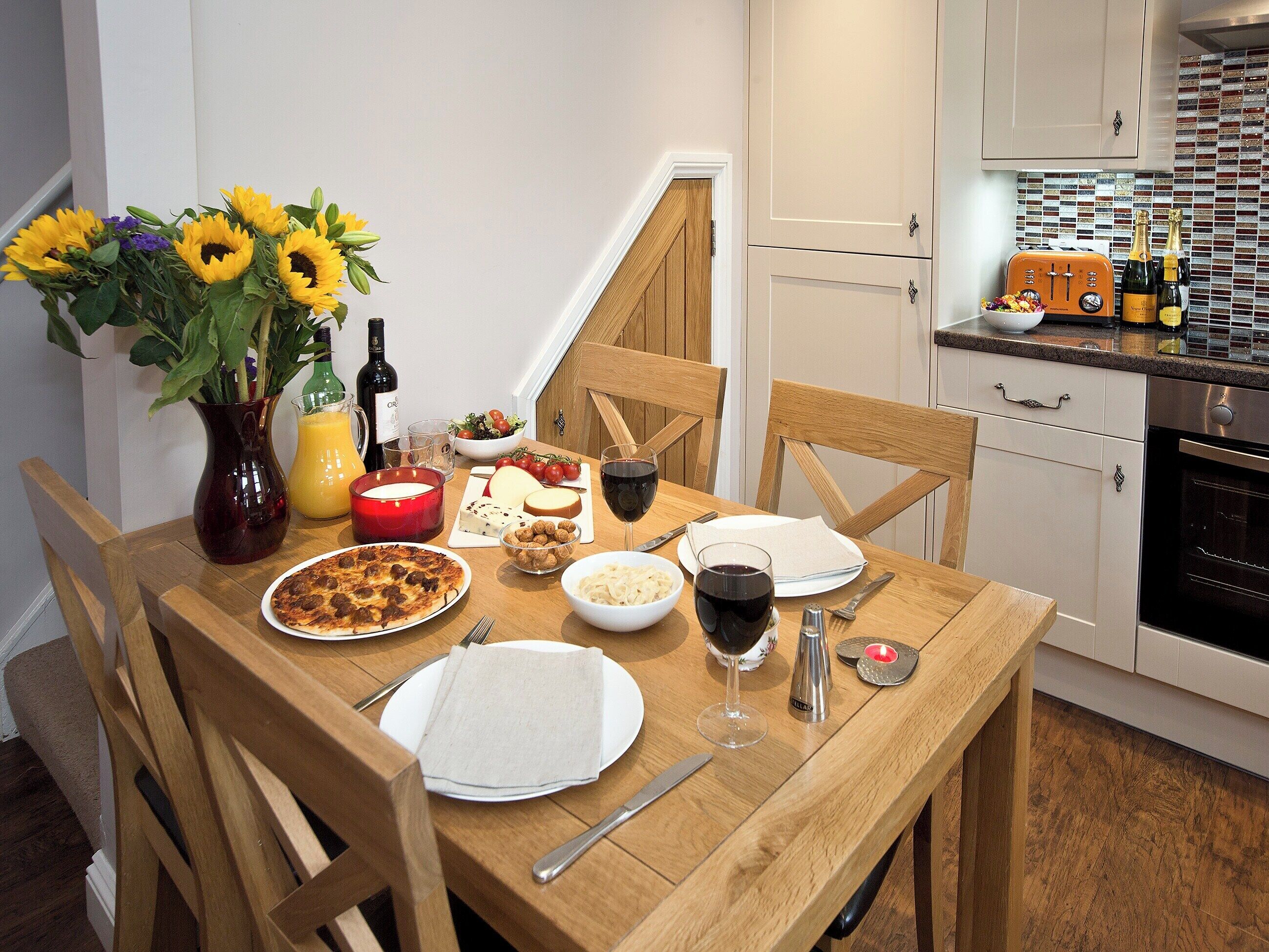 A dining table set with food, wine, and a vase of sunflowers.