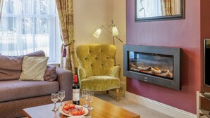 A living room with a sofa, armchair, fireplace, and a bottle of wine on a table. - 3 bedroom accommodation in Keswick (Keswick)