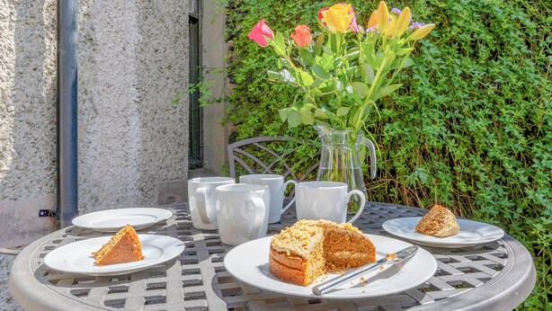 A round metal table with plates of cake, white mugs, and a pitcher of water. - 3 bedroom accommodation in Keswick (Keswick)