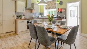 A modern kitchen with a dining area, featuring a central island, pendant lights, and a view of the outdoors. - 3 bedroom accommodation in Keswick (Keswick)