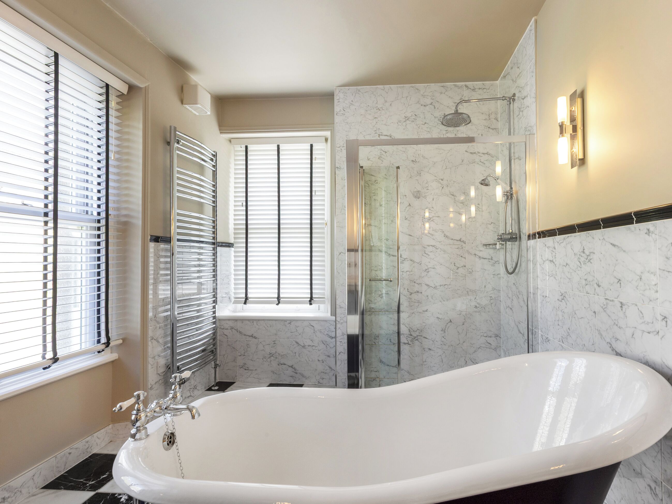 A bathroom with a freestanding bathtub, a glass-enclosed shower, and a window with blinds.