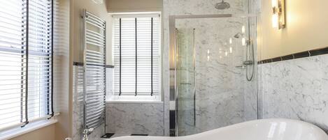 A bathroom with a freestanding bathtub, a glass-enclosed shower, and a window with blinds.