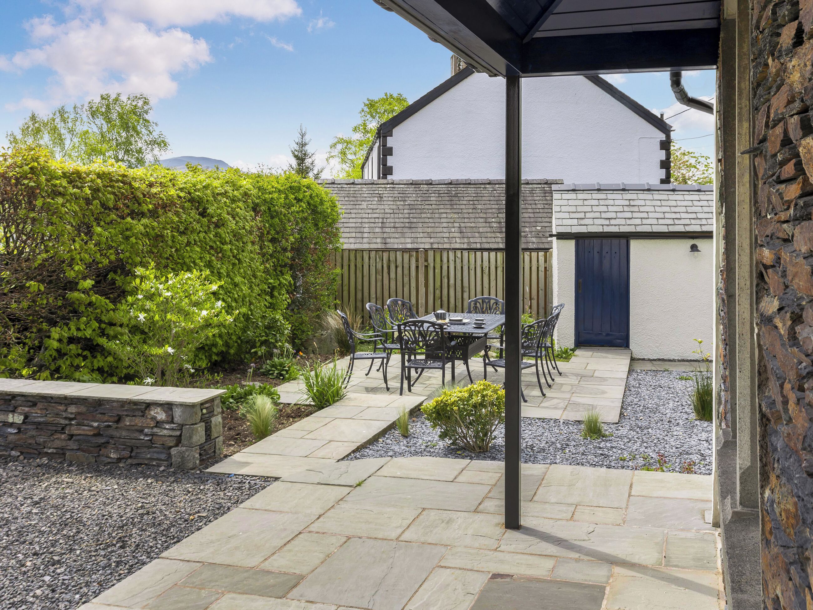 A patio with a table and chairs, a stone pathway, and a building with a blue door.