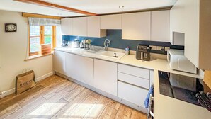 A modern kitchen with white cabinets, a wooden countertop, a sink, and a window with curtains. - 2 bedroom accommodation in Pooley Bridge (Pooley Bridge)