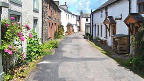 A narrow street lined with traditional stone and plaster houses, a cobblestone path, and blooming pink roses. - 2 bedroom accommodation in Pooley Bridge (Pooley Bridge)