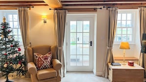 Een gezellige woonkamer met een houten plafond, een comfortabele fauteuil, een kerstboom, en een deur die naar buiten leidt.