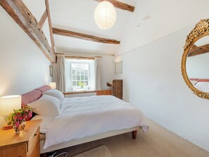 Un dormitorio con cama, mesita de noche, ventana con cortinas, viga de techo de madera y espejo en la pared.