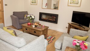 Ein Wohnzimmer mit einer Couch, einem Couchtisch mit Kerzen, einem Flachbildfernseher und einem Kamin.