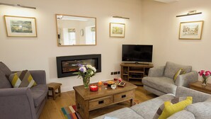Ein Wohnzimmer mit grauen Sofas, einem Flachbildfernseher, einem Kamin und gerahmten Bildern an der Wand.