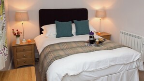 Ein ordentlich bezogenes Bett mit einer Karodecke, zwei Nachttische mit Lampen, ein Beistelltischchen mit einer Kerze und eine Heizung.