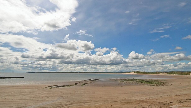 En strand med et stort sandområde, roligt vand og delvist overskyet himmel.