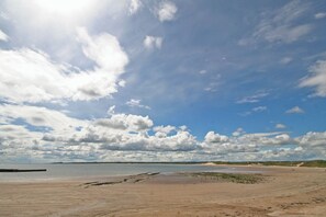 A beach with a wide sandy area, a body of water, and distant dunes under a partly cloudy sky. - 3 bedroom accommodation in Beadnell (Beadnell)