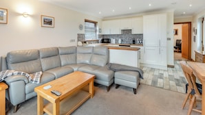 A modern living room with a sectional sofa, a wooden coffee table, and a dining area with a wooden table and chairs. - 1 bedroom accommodation in Red Row near Amble (Red Row near Amble)