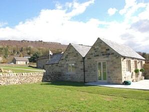 A stone building with a pitched roof, a flag, and a stone wall in a grassy area. - 2 bedroom accommodation in Froggatt near Bakewell (Froggatt near Bakewell)