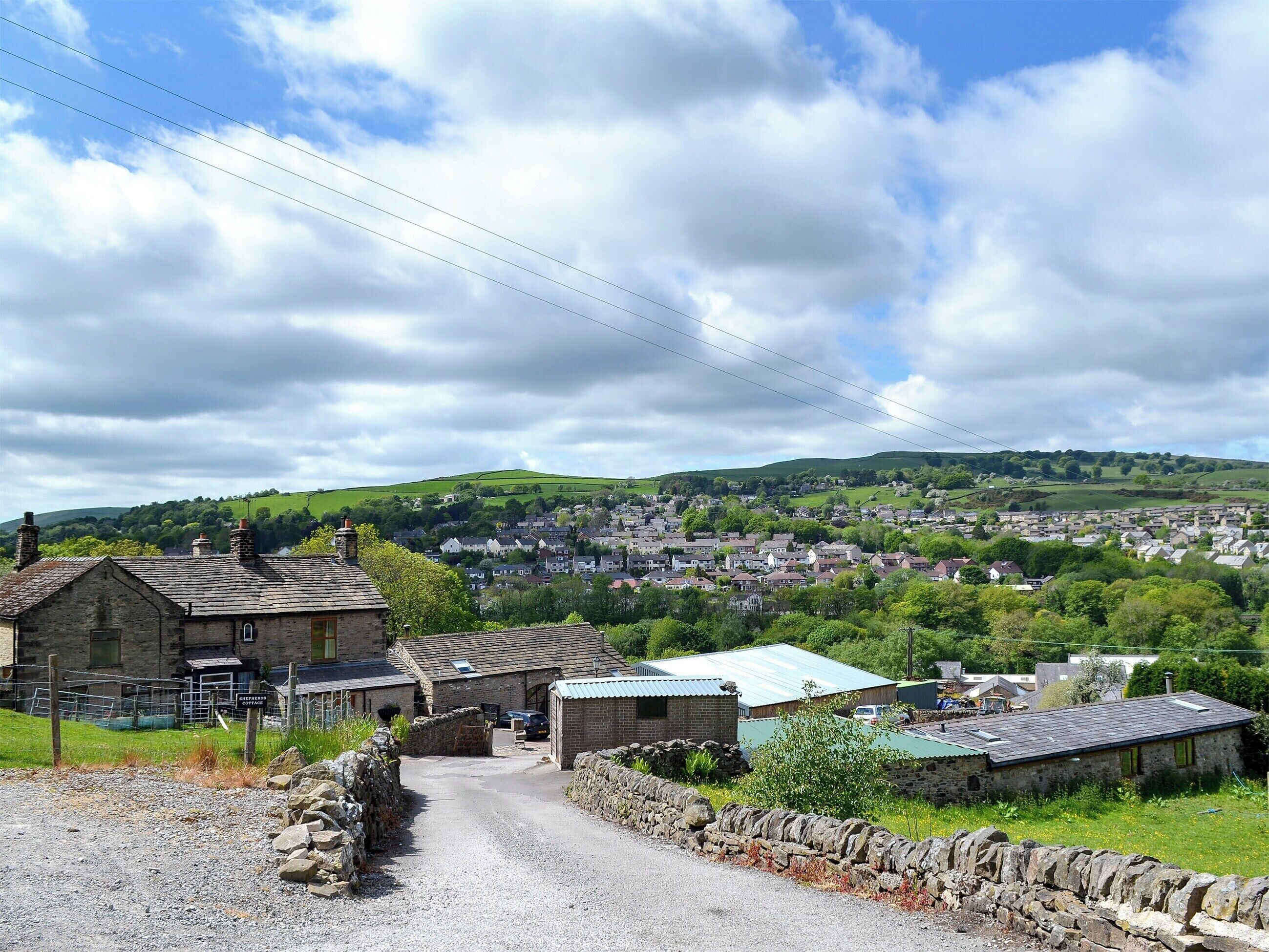 A rural village with stone buildings, a gravel road, and a view of a larger town in the distance.
