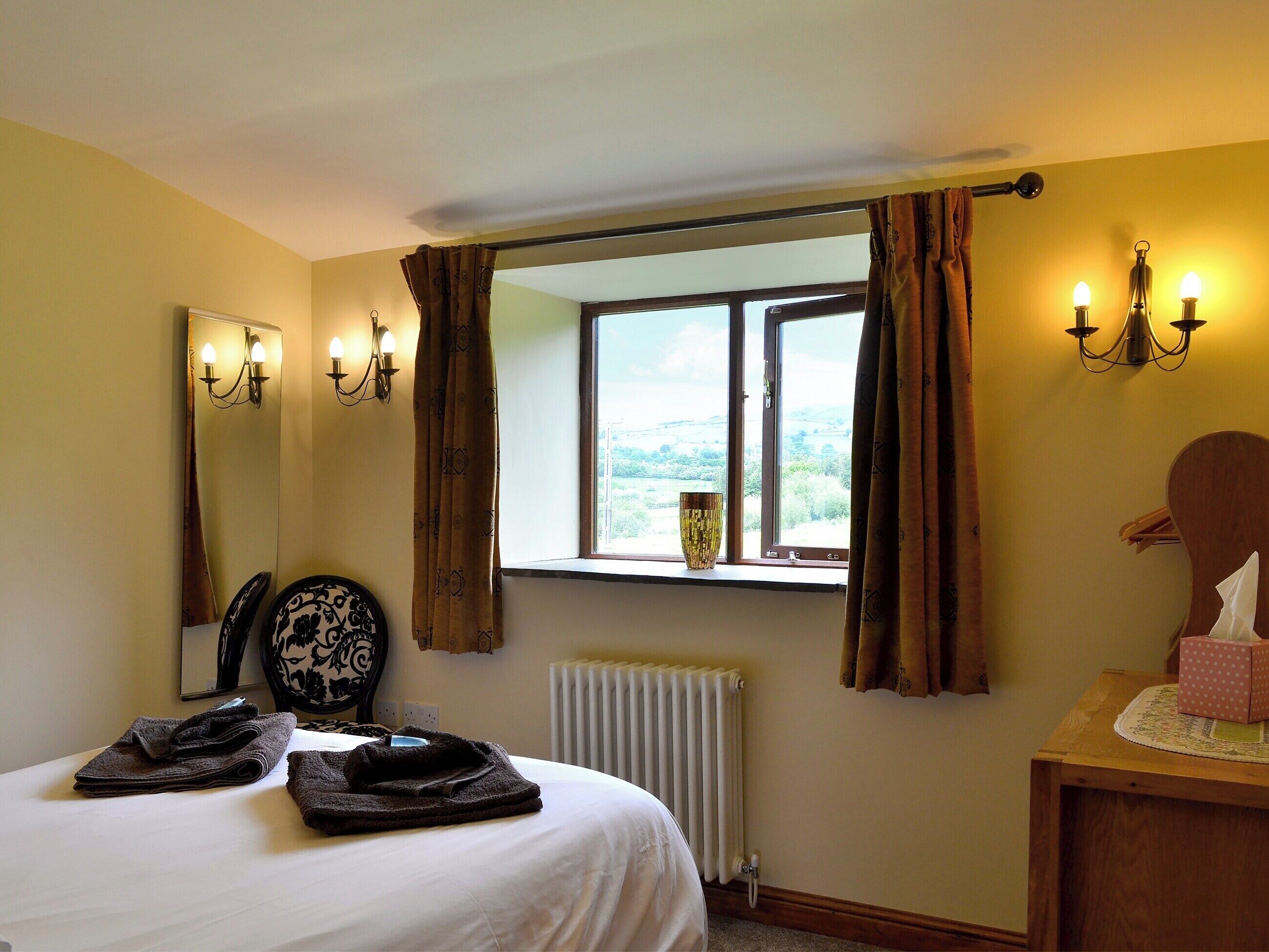 A bedroom with a bed, a window with curtains, a radiator, a mirror, and wall sconces.