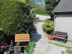 Een tuinpad dat leidt naar een gebouw met een bank en een rode emmer.