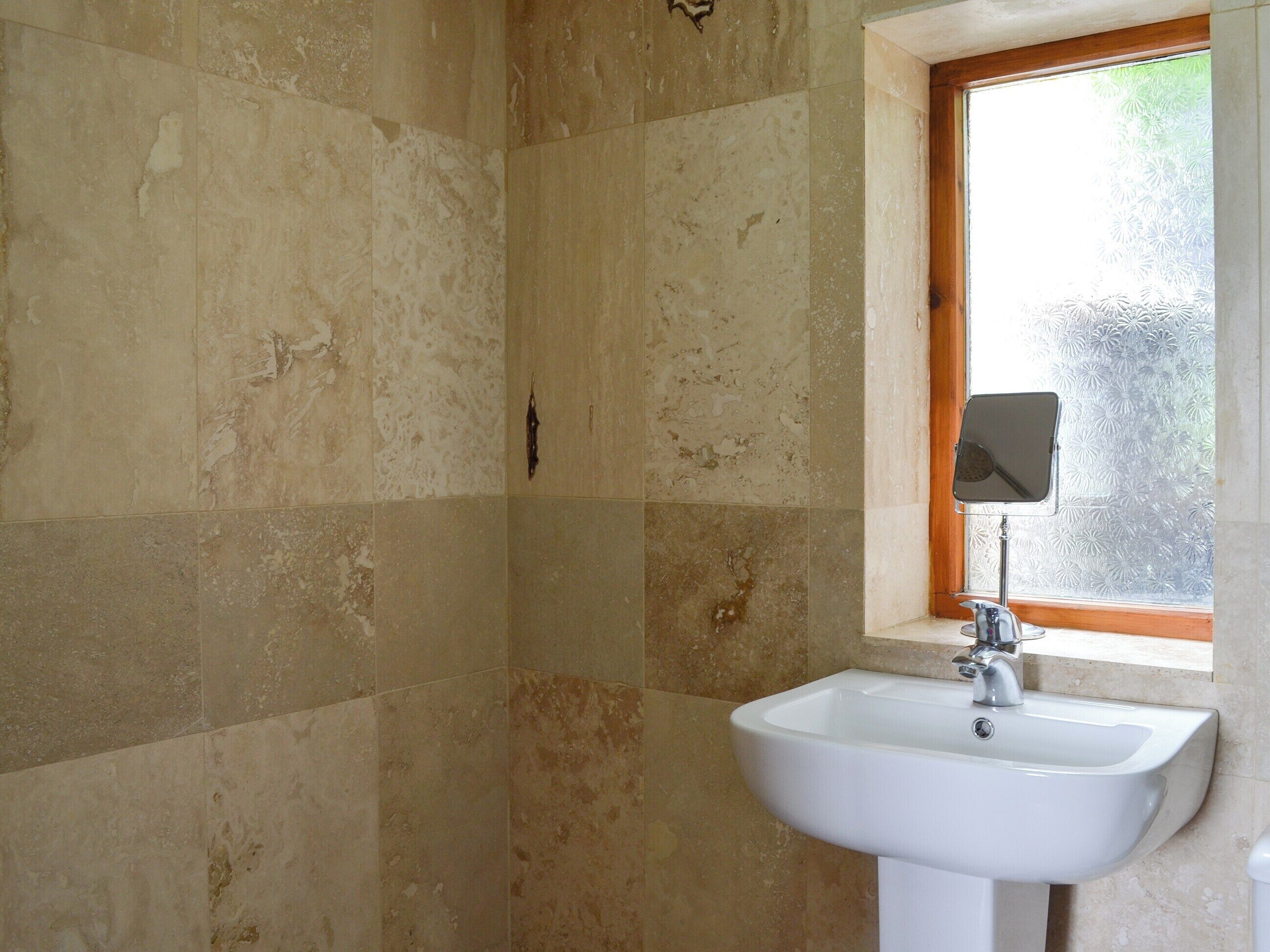 A bathroom with a white sink, a mirror, and a window with frosted glass.