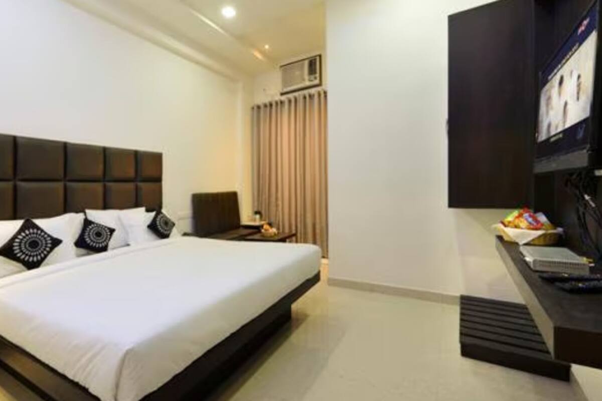 A modern hotel room with a large bed, a bedside table, a mirror, a TV, and a wardrobe.