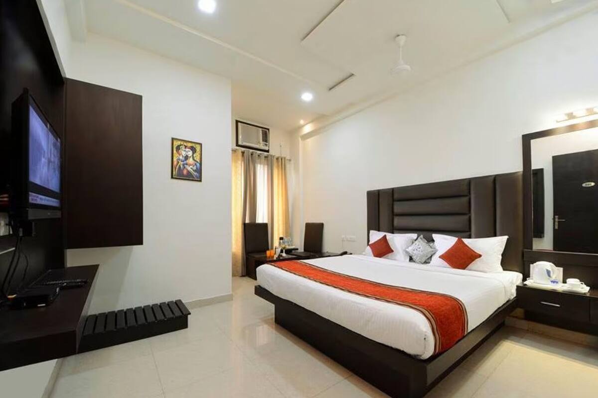 A modern hotel room with a large bed, a desk with a computer, a television, and a large mirror.