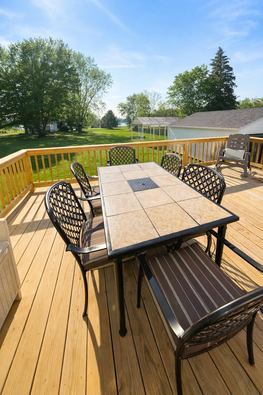 Une terrasse en bois avec une table et des chaises, entourée d’une rambarde, donnant sur une pelouse et un bâtiment.