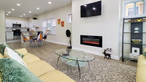 Un salon moderne avec une table basse en verre, un canapé, une cheminée et une cuisine en arrière-plan.