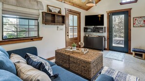 A cozy living room with a blue sofa, wicker ottoman, and a television. - Private Hot Tub & Dock! Lakefront Log Cabin Oasis (Onalaska)