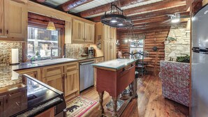 A rustic kitchen with wooden cabinets, a stone wall, and a wooden dining table with chairs. - Private Hot Tub & Dock! Lakefront Log Cabin Oasis (Onalaska)