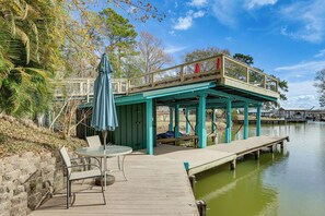 A wooden dock extending into a calm body of water, with a covered seating area and a table with chairs. - Private Hot Tub & Dock! Lakefront Log Cabin Oasis (Onalaska)