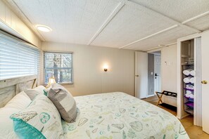 Ein Schlafzimmer mit einem Bett, einem Fenster mit Jalousien, einem Nachttisch, einer Wandlampe und einem Kleiderschrank mit Regalen.