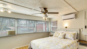 Un dormitorio con cama, ventilador de techo, aire acondicionado y ventanas con persianas.