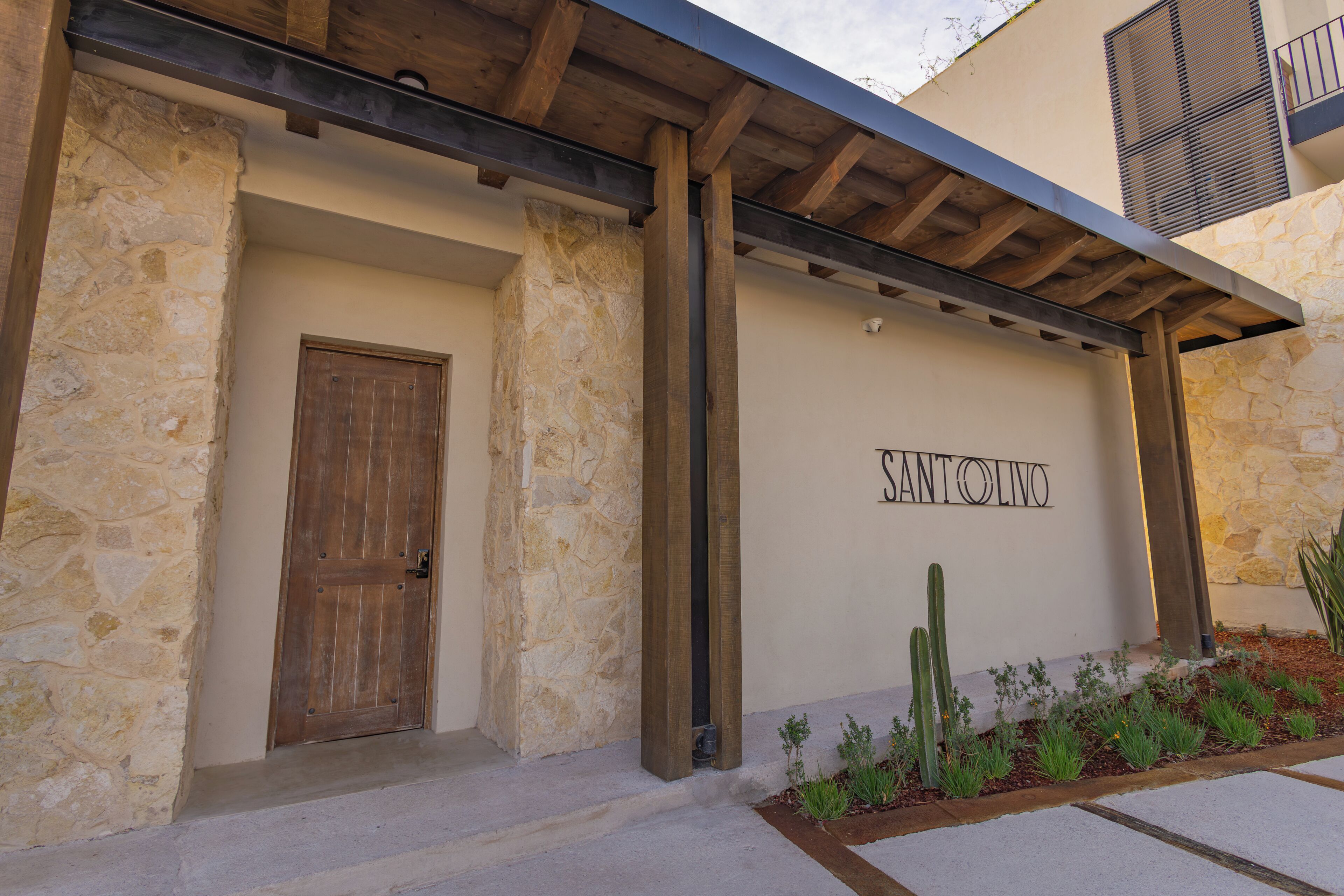 A building entrance with a stone facade, a wooden door, and the name 'SANTOLIVO' on the wall.