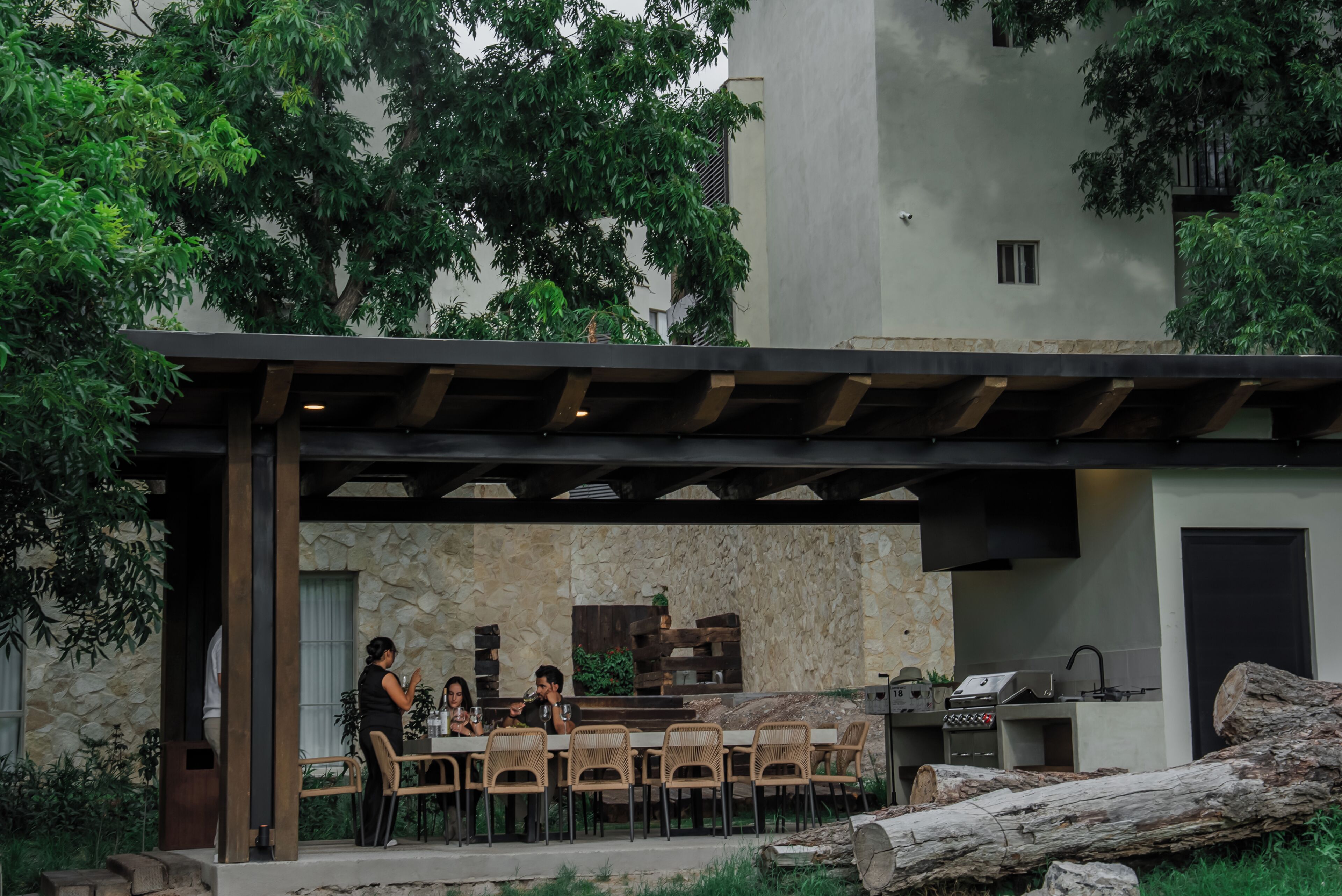 Uma área de refeições ao ar livre com um painel de parede de pedra, pérgola de madeira e estação de churrasco.