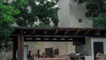 Uma área de refeições ao ar livre com um painel de parede de pedra, pérgola de madeira e estação de churrasco.